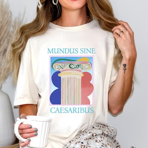 Könnte beinhalten: Ein weißes T-Shirt mit einem Grafikdruck einer bunten Säule mit dem Text "MUNDUS SINE CAESARIBUS" auf der Vorderseite.