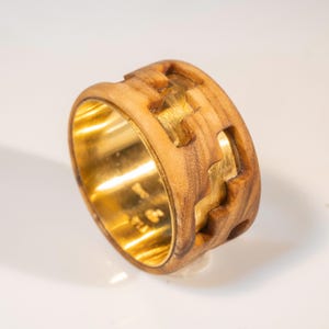 Könnte beinhalten: Ein Holzring mit einem goldenen Band und einem einzigartigen Design. Der Ring ist aus Olivenholz gefertigt und hat eine natürliche Holzmaserung.