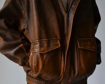 May include: A brown leather bomber jacket with a zip-up front, two front pockets, and a ribbed hem. The jacket has a classic collar and shoulder epaulets. The leather has a distressed look.
