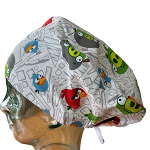 May include: A white scrub hat with a colorful Angry Birds print. The hat has a white drawstring.