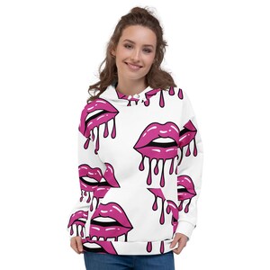 May include: White hoodie with a repeating pattern of pink lips with dripping accents. The lips have a glossy finish and are outlined in black. The hoodie has a drawstring hood and a front pocket.