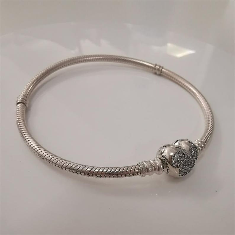 May include: A silver-colored bracelet with a snake chain design. The bracelet features a heart-shaped clasp adorned with small, sparkling stones. The bracelet is a piece of jewelry.