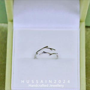Op de afbeelding: Een zilverkleurige ring met een takachtig ontwerp, gepresenteerd in een witte doos in een groene sieradendoos. De delicate takken van de ring buigen sierlijk. De tekst "HUSSAIN 2024 Handcrafted Jewellery" is zichtbaar onderaan.