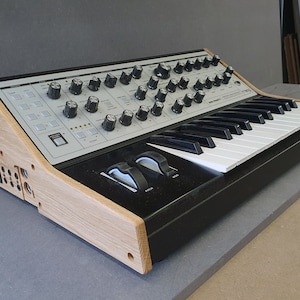 May include: A black and white synthesizer with a wooden stand. The synthesizer has a keyboard with 37 keys and a variety of knobs and buttons.