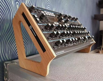 May include: A wooden stand for a Novation Summit synthesizer. The stand is made of light brown wood and has a triangular shape. The synthesizer is black with blue accents and has the text "Summit Analog Synthesizer" printed on the front.