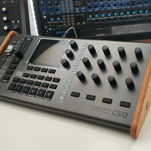 Puede incluir: Un controlador DAW Nektar Panorama CS12 Chrome con un panel lateral de madera. El controlador tiene una pantalla, botones y perillas.