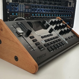 Puede incluir: Un controlador de producci&oacute;n musical negro con un soporte de madera. El controlador tiene una pantalla grande, botones, botones y faders. El texto "nektar" est&aacute; impreso en la parte frontal del controlador.