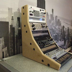 Puede incluir: Un soporte de madera beige con un sintetizador en la parte superior. El sintetizador tiene un diseño plateado y negro con perillas y botones. El soporte tiene una superficie texturizada y está hecho de madera.