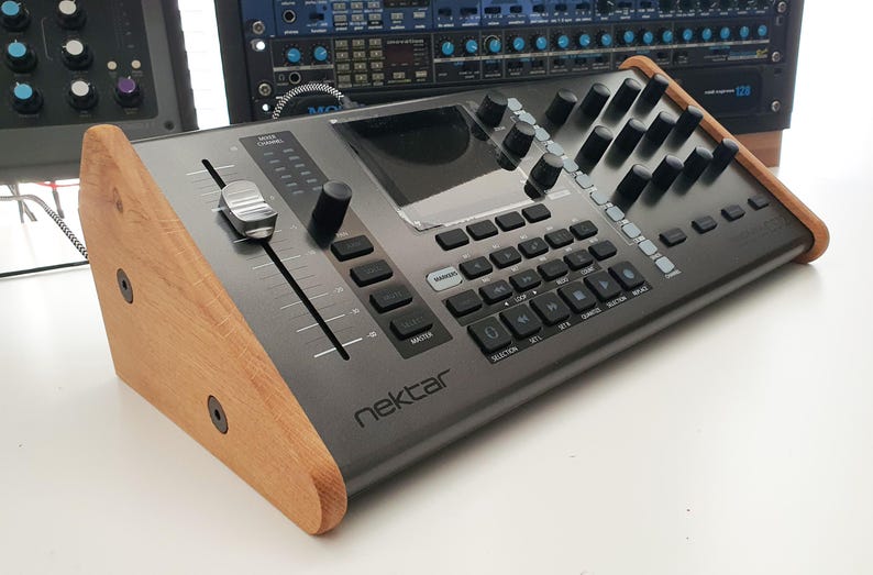 Puede incluir: Un controlador de producci&oacute;n musical negro con un soporte de madera. El controlador tiene una pantalla grande, botones, botones y un fader. El texto "nektar" est&aacute; impreso en la parte frontal del controlador.