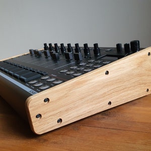 以下が含まれることがあります： 黒い電子音楽サンプラーと木製スタンド。スタンドは薄い茶色の木でできており、いくつかのネジが見える