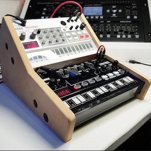 May include: A wooden stand with two Korg Volca synthesizers. The top synthesizer is white with a red digital display and the text "volca sample". The bottom synthesizer is black with a red digital display and the text "volca kick".