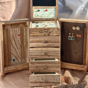 May include: A wooden jewellery organiser with multiple compartments and drawers. The organiser has a natural wood finish and includes a mirror, ring holders, earring displays, and necklace hooks. The name "Kristy Humbert" is visible on the front.