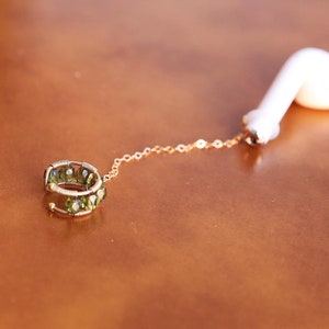 Puede incluir: Una cadena de oro con un anillo de piedras preciosas verdes unido a un auricular blanco.