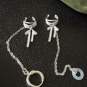 Puede incluir: Puños de oreja plateados con cadenas. Uno tiene un lazo, el otro un anillo transparente. El texto en la imagen dice "For loop earplug" y "For earbud". Los puños tienen un diseño de lazo.