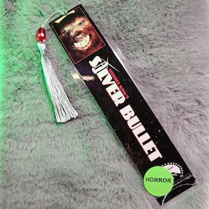 May include: A black and silver bookmark with a werewolf illustration and the text "Stephen King's Silver Bullet". The bookmark has a red and silver tassel and a green circle with the word "HORROR" on it.