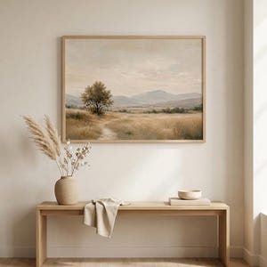 Puede incluir: Un cuadro de paisaje rectangular en un marco de madera clara que representa un campo de hierba, un árbol solitario y montañas lejanas bajo un cielo suave. La obra cuelga sobre un banco de madera clara con un jarrón beige y un cuenco.