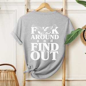May include: Gray t-shirt with a white graphic print that says "F**k Around and Find Out" with a stylized eagle design.