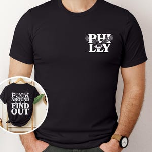 May include: Black t-shirt with a white eagle graphic and the text "PHILLY" on the front. The back of the shirt has the text "F**K AROUND AND FIND OUT".