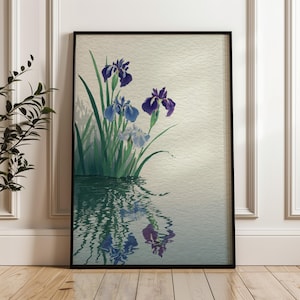 Puede incluir: Una impresión artística enmarcada que presenta una pintura de acuarela de lirios. Los lirios están representados en tonos de morado y azul, con hojas y tallos verdes. Las flores se reflejan en el agua de abajo, creando una escena serena y artística.