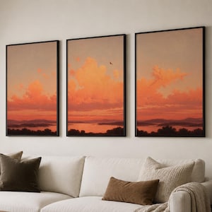 Könnte beinhalten: Ein Triptychon aus drei gerahmten Wandbildern, die eine Landschaft bei Sonnenuntergang zeigen. Jeder vertikale rechteckige Druck zeigt orangefarbene und rosafarbene Wolken über einer dunklen Silhouette von Bergen und einem Gewässer.