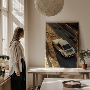 A vintage Porsche 911 captured in warm golden-hour light, highlighting the car's sleek curves and classic design. The automotive wall art print features nostalgic shadows and earthy tones, perfect for car enthusiasts. Displayed on a table in a bright, minimalist living space.