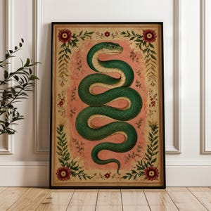 Puede incluir: Una lámina de arte mural rectangular enmarcada que muestra una serpiente verde enroscada con el vientre color crema, centrada sobre un fondo rosa texturizado. La ilustración está rodeada por un borde decorativo de hojas verdes y flores rojas.