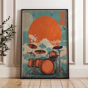 May include: A framed poster featuring a drum kit set against a stylized landscape with a large orange sun, a snow-capped mountain, and blue waves. The artwork includes orange Japanese characters in the upper right corner and a weathered texture.