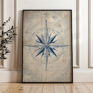 Peut inclure: Impression encadrée représentant une rose des vents bleue détaillée sur un fond de carte vintage. La rose des vents, avec ses lignes complexes et son motif en étoile, est le point central. L'impression est encadrée dans un cadre noir, pour une décoration nautique ou sur le thème du voyage.