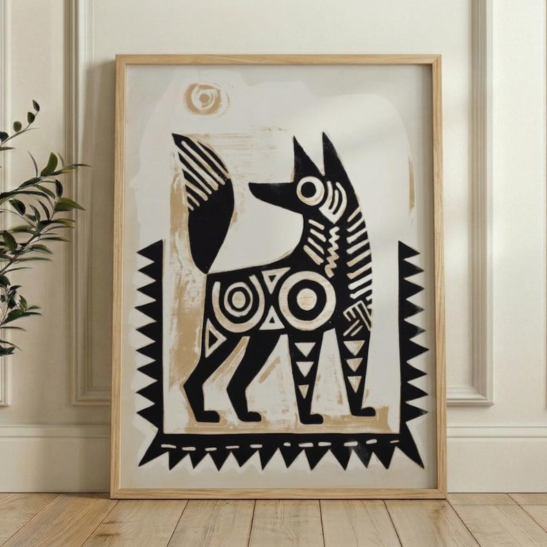 A man is holding a framed artwork of a stylized dog or fox, which is hanging on a wall.
