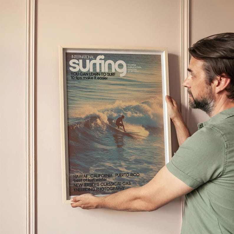 Vintage coastal surf poster featuring a lone surfer riding a golden wave in soft pastel ocean hues with classic magazine cover typography. The retro surfing art print captures a timeless beach vibe full of adventure and nostalgia. Displayed in a softly lit, modern living space.