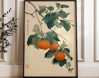May include: Framed art print featuring a branch with green leaves and vibrant orange persimmons. The artwork has Japanese text and a red seal. The print is set against a beige background and framed in black.