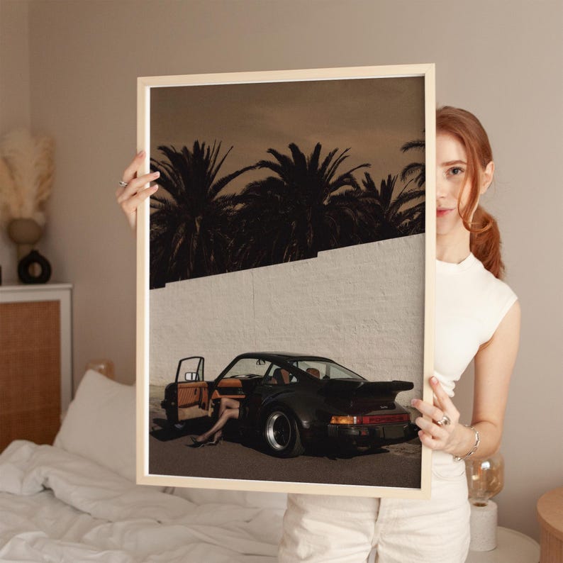 A vintage black Porsche sports car with an open door and a figure’s legs visible, set against a white wall and silhouetted palm trees in moody, warm tones. The cinematic retro poster captures a sleek, nostalgic vibe. Displayed in a cozy bedroom environment.