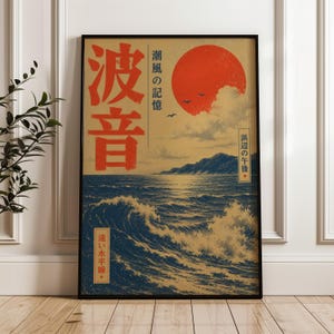 May include: A framed rectangular wall art print featuring a stylized ocean scene with dark blue waves, a tan sky, and a large red sun. The print includes Japanese text characters in red and black, with small silhouettes of birds flying near the sun.