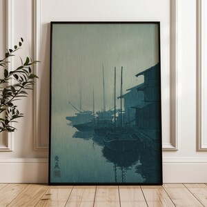 May include: A framed vertical wall art print featuring a monochromatic blue-toned scene of several wooden boats moored along a dock next to traditional buildings. The artwork displays a misty atmosphere with vertical texture lines and Japanese calligraphy.