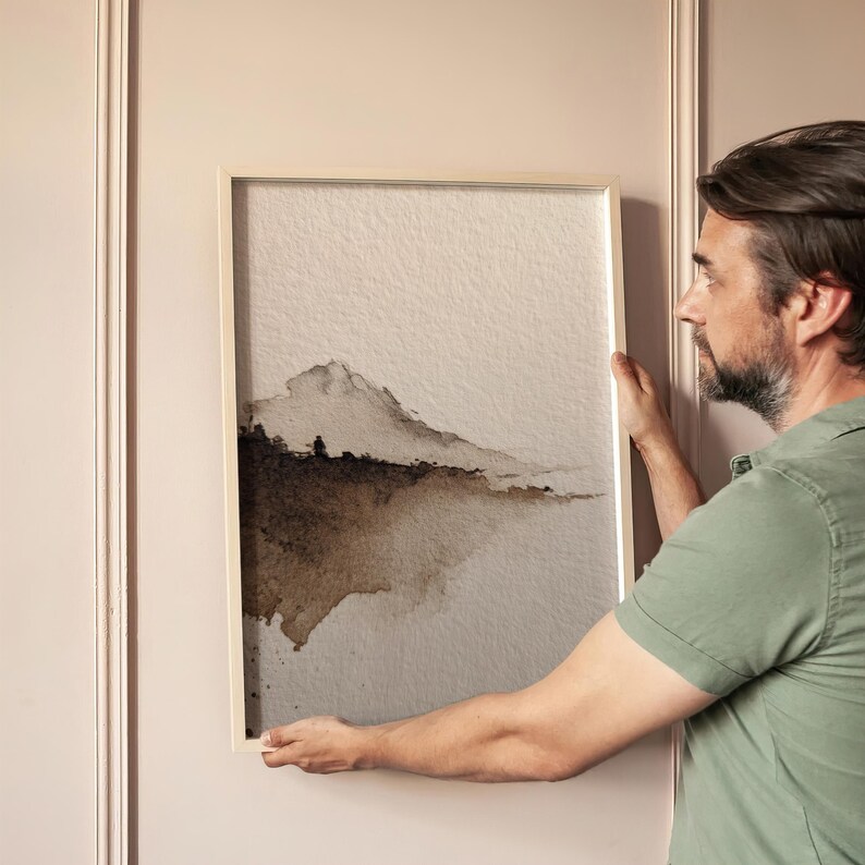 Abstract landscape watercolor art print in earthy brown tones with a minimal wabi-sabi style, emphasizing natural imperfection. The serene composition features soft edges and a subtle gradient on textured paper. Displayed against a neutral wall, perfect for calming and minimalist interior decor.