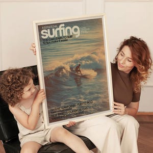 A vintage-style surf poster featuring a lone surfer riding a sunlit wave in soft pastel ocean tones with retro typography. The art print evokes a nostalgic coastal vibe perfect for beach house décor. Displayed in a warm, inviting living room setting.
