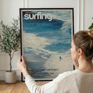 A vintage-style surf poster featuring a lone surfer catching a large ocean wave in cool blue tones. The artwork captures the dynamic energy of the sea with a nostalgic coastal vibe. Displayed in a serene home setting, adding beach-inspired wall art charm.
