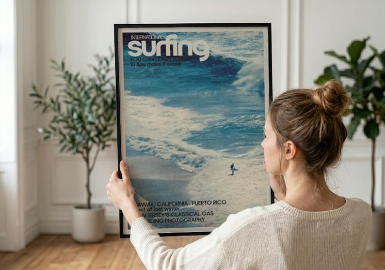 A vintage-style surf poster featuring a lone surfer catching a large ocean wave in cool blue tones. The artwork captures the dynamic energy of the sea with a nostalgic coastal vibe. Displayed in a serene home setting, adding beach-inspired wall art charm.