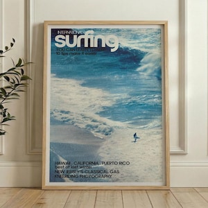 A vintage-style surf poster featuring a lone surfer navigating a large ocean wave in shades of blue and white. The artwork has a nostalgic, retro surf magazine cover look. Displayed framed in a bright, modern living space.