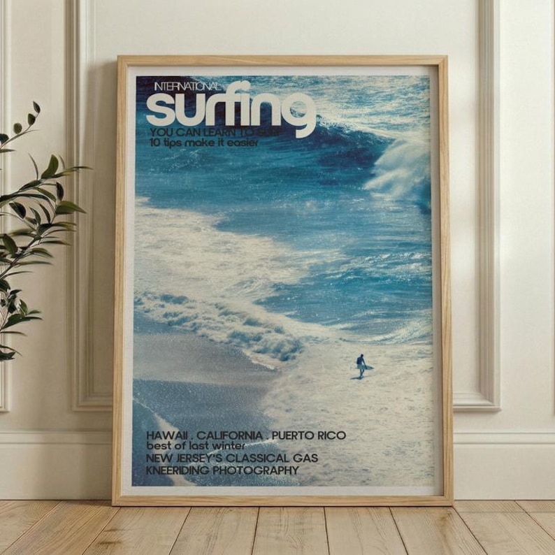 A vintage-style surf poster featuring a lone surfer navigating a large ocean wave in shades of blue and white. The artwork has a nostalgic, retro surf magazine cover look. Displayed framed in a bright, modern living space.