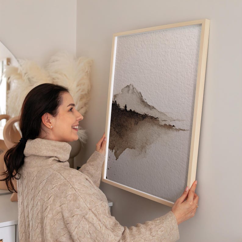 Abstract landscape watercolor artwork in earthy brown tones captures a minimal wabi-sabi aesthetic with soft gradient and textured paper. The serene, natural imperfection creates calming wall art perfect for rustic or minimalist decor. Displayed in a cozy contemporary living space, it adds a peaceful, understated touch.