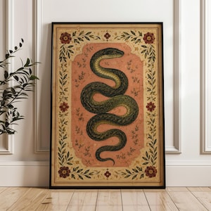 May include: A framed rectangular wall art print featuring a coiled dark green snake centred on a muted pink background. The central panel is surrounded by a decorative border of green leaves and small red flowers on a cream-coloured parchment.