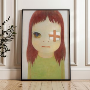 May include: Framed art print featuring a stylized portrait of a young girl with red hair and a green shirt. One eye is detailed with colorful patterns, while the other is covered by a bandage. The artwork is framed in a black border.