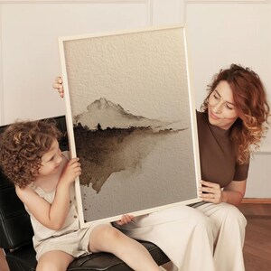 Minimalist abstract landscape art in earthy brown and beige tones with a wabi-sabi style, featuring a subtle watercolor wash on textured paper. The serene and calming fine art print is held by a woman and child in a cozy living space. This poster complements minimalist and rustic interiors with its natural, understated aesthetic.