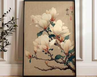 Puede incluir: Una impresión enmarcada con una ilustración botánica de flores de magnolia. La obra de arte muestra flores de color blanco cremoso con toques de rosa y verde sobre un fondo beige. La impresión está en un marco negro y tiene texto japonés.