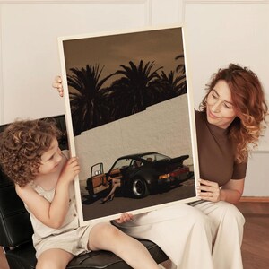 Moody vintage Porsche sports car wall art print in muted warm tones, featuring an open door and silhouetted palm trees. The retro cinematic poster creates a sophisticated, nostalgic vibe. Displayed in a cozy living room setting.