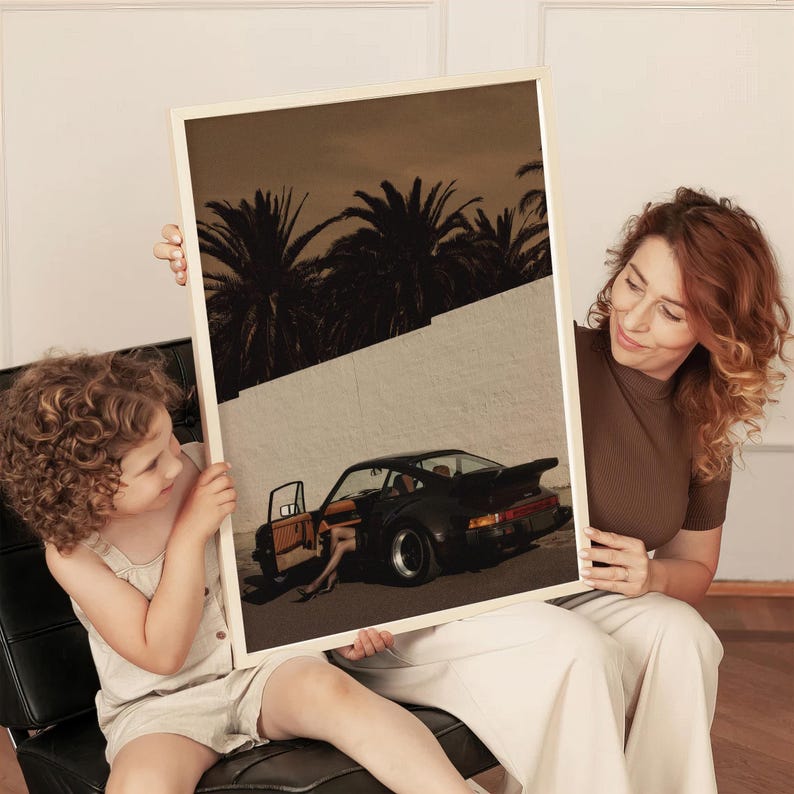 Moody vintage Porsche sports car wall art print in muted warm tones, featuring an open door and silhouetted palm trees. The retro cinematic poster creates a sophisticated, nostalgic vibe. Displayed in a cozy living room setting.