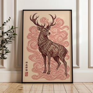 May include: A framed wall art print featuring a detailed dark brown ink illustration of a standing stag with large antlers. The deer is set against a background of swirling, dusty rose-colored clouds. Vertical Japanese text and a red seal are visible.