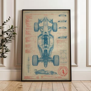 May include: Framed blueprint-style print of a Formula 1 race car. The artwork features a detailed top-down view of the car in blue lines, with additional diagrams and text in red. The print is displayed in a black frame.