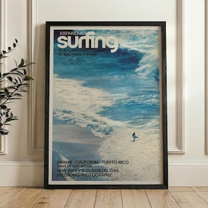 Vintage style surf poster featuring a lone surfer riding a large ocean wave in shades of blue and white. The nostalgic coastal print captures the energy and beauty of the sea with a retro magazine cover design. Displayed in a calm bedroom setting, it adds adventure and tranquility to beach-themed decor.